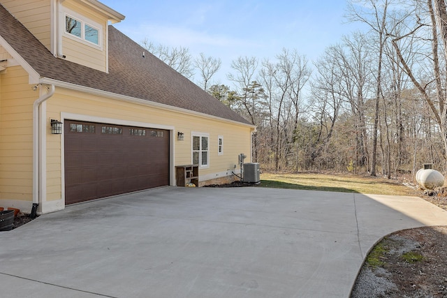 view of side of property with central AC unit, driveway, and roof with shingles