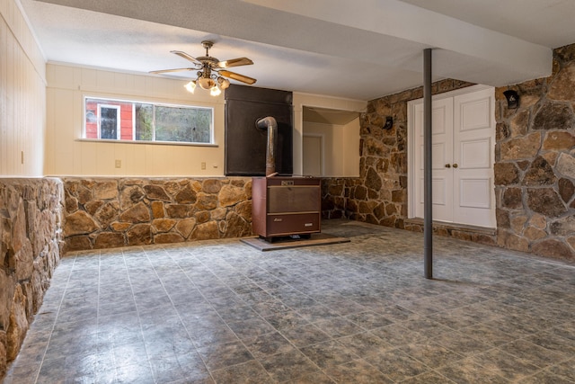 unfurnished living room featuring ceiling fan and a wood stove