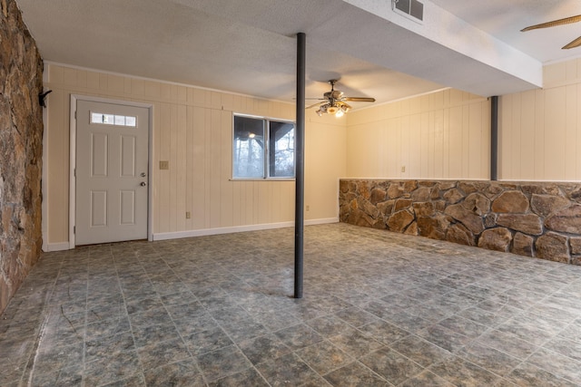 basement with ceiling fan and wooden walls