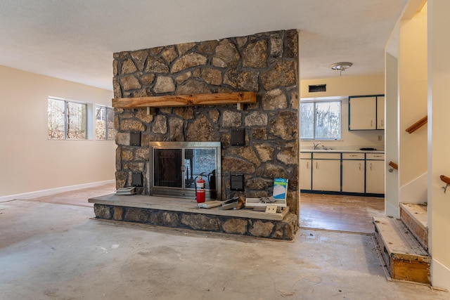 living room with a textured ceiling, a stone fireplace, sink, and a wealth of natural light