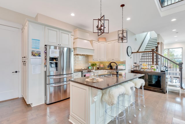 kitchen featuring premium range hood, a breakfast bar area, stainless steel appliances, dark stone countertops, and sink