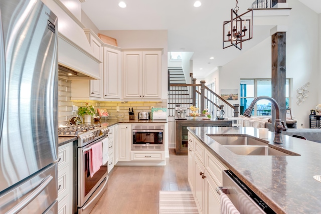 kitchen with pendant lighting, stainless steel appliances, sink, backsplash, and light hardwood / wood-style flooring