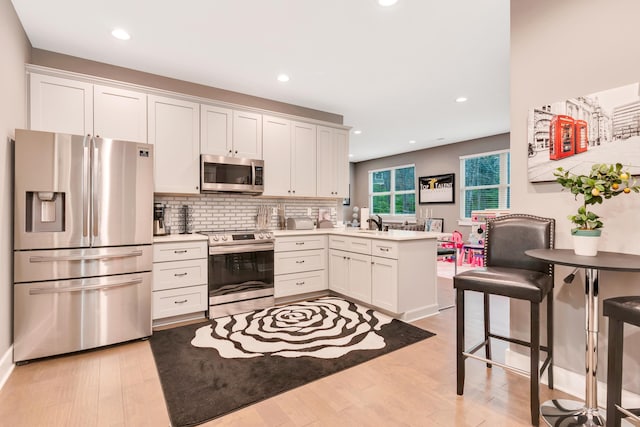 kitchen with white cabinets, stainless steel appliances, light hardwood / wood-style floors, kitchen peninsula, and a breakfast bar area