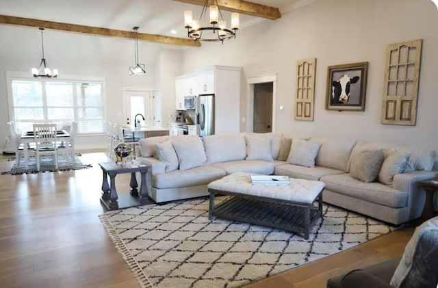 living room featuring beam ceiling, light wood-type flooring, a high ceiling, and a notable chandelier