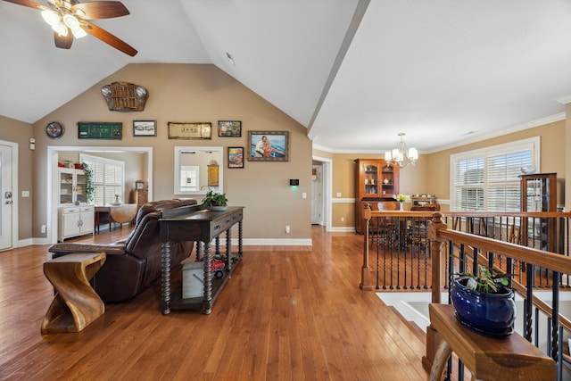 living room featuring ceiling fan with notable chandelier, hardwood / wood-style flooring, vaulted ceiling, and crown molding