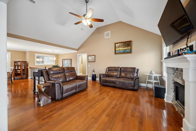 living room featuring hardwood / wood-style floors, ceiling fan, a stone fireplace, and lofted ceiling