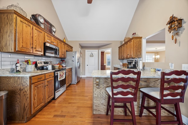 kitchen featuring kitchen peninsula, appliances with stainless steel finishes, a kitchen bar, tasteful backsplash, and light stone countertops