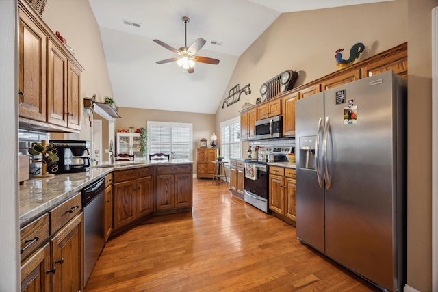 kitchen featuring ceiling fan, light stone countertops, light hardwood / wood-style flooring, decorative backsplash, and appliances with stainless steel finishes