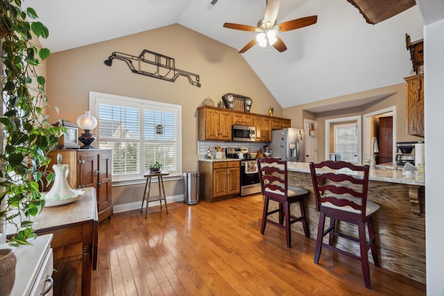 kitchen with appliances with stainless steel finishes, tasteful backsplash, vaulted ceiling, ceiling fan, and light hardwood / wood-style floors