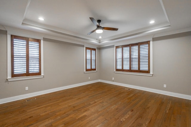 empty room with ceiling fan, a raised ceiling, and wood-type flooring