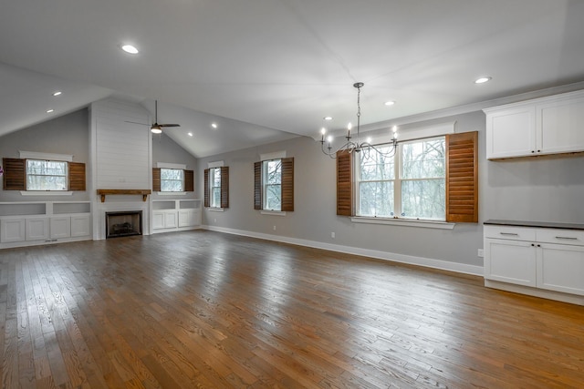 interior space with hardwood / wood-style flooring, ceiling fan with notable chandelier, a large fireplace, and lofted ceiling