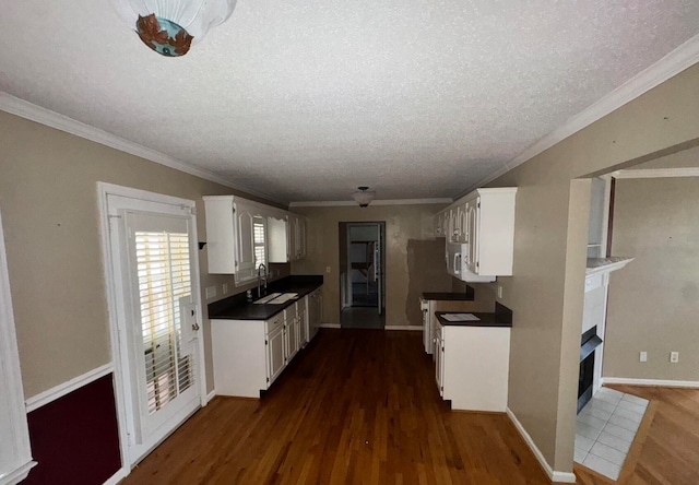 kitchen featuring white cabinets, sink, dark hardwood / wood-style floors, a textured ceiling, and a tiled fireplace