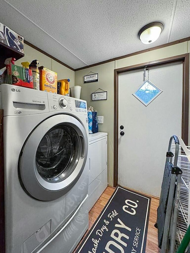 laundry area featuring ornamental molding, separate washer and dryer, light hardwood / wood-style flooring, and a textured ceiling