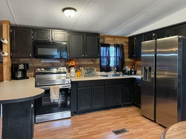 kitchen featuring sink, appliances with stainless steel finishes, light hardwood / wood-style floors, vaulted ceiling, and kitchen peninsula