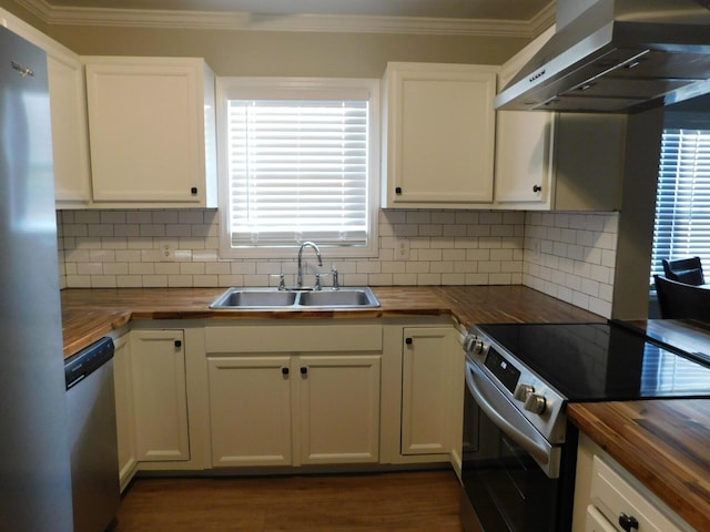 kitchen featuring wood counters, appliances with stainless steel finishes, wall chimney exhaust hood, sink, and white cabinets