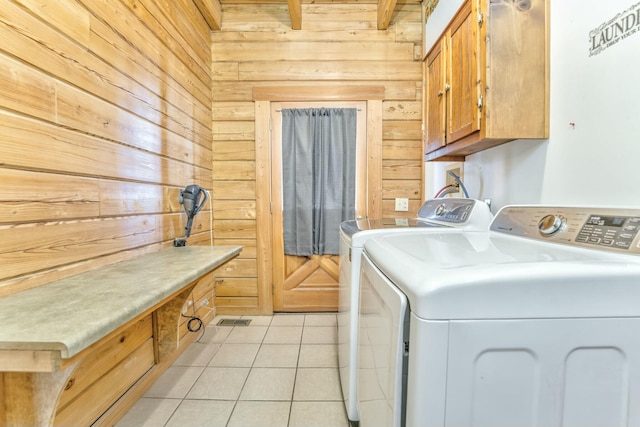 clothes washing area featuring light tile patterned floors, wood walls, washing machine and clothes dryer, and cabinets