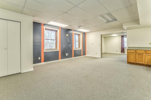 basement featuring a healthy amount of sunlight, a paneled ceiling, and light colored carpet