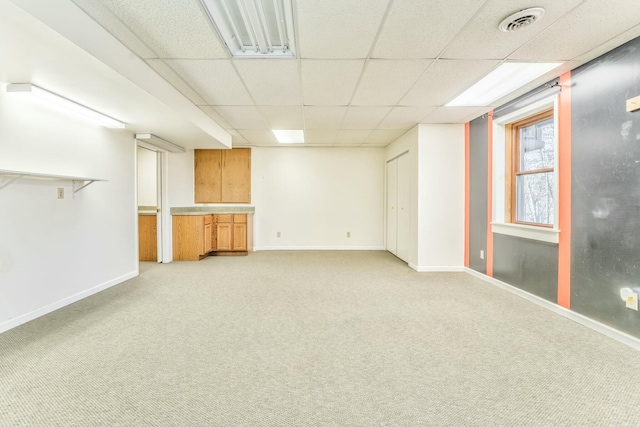 basement featuring a paneled ceiling and light carpet