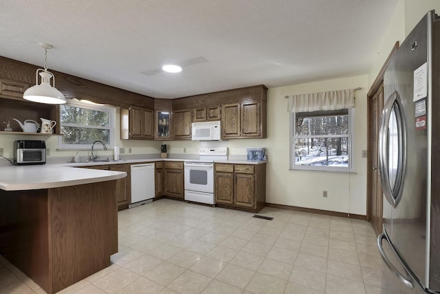 kitchen with pendant lighting, sink, white appliances, a textured ceiling, and kitchen peninsula