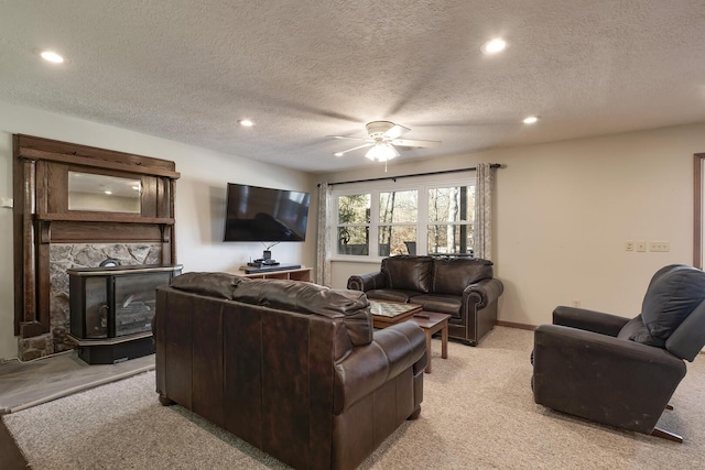 carpeted living room featuring ceiling fan, a stone fireplace, and a textured ceiling