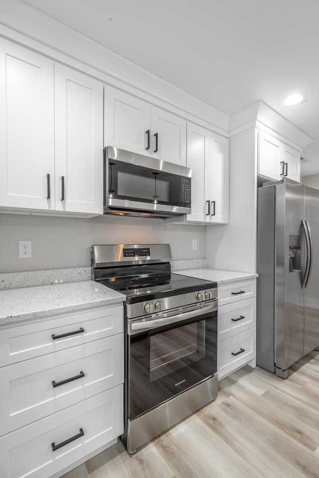 kitchen with light hardwood / wood-style floors, light stone counters, white cabinetry, and appliances with stainless steel finishes