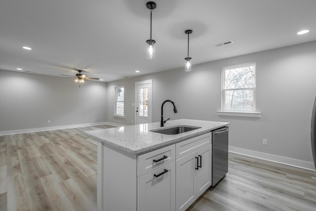 kitchen with light stone counters, a kitchen island with sink, sink, decorative light fixtures, and white cabinets