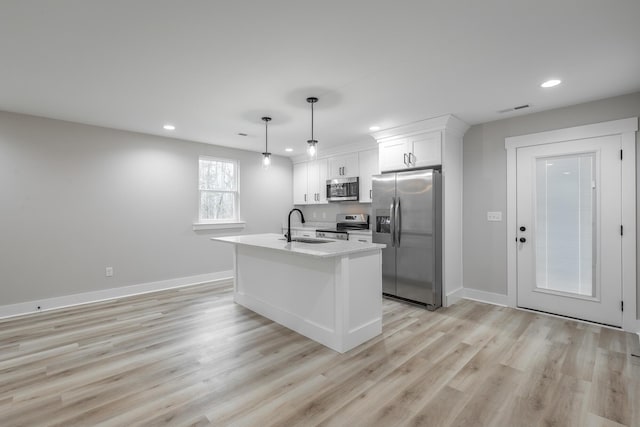 kitchen with stainless steel appliances, a kitchen island with sink, sink, pendant lighting, and white cabinetry