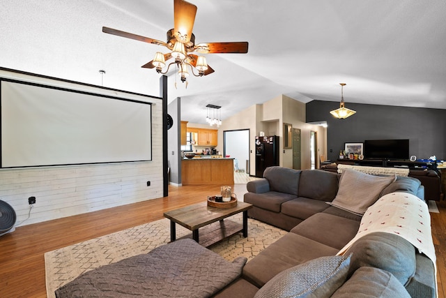 cinema room featuring ceiling fan with notable chandelier, wooden walls, light hardwood / wood-style flooring, and lofted ceiling