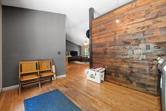 living area featuring washer / clothes dryer, wooden walls, hardwood / wood-style floors, and vaulted ceiling