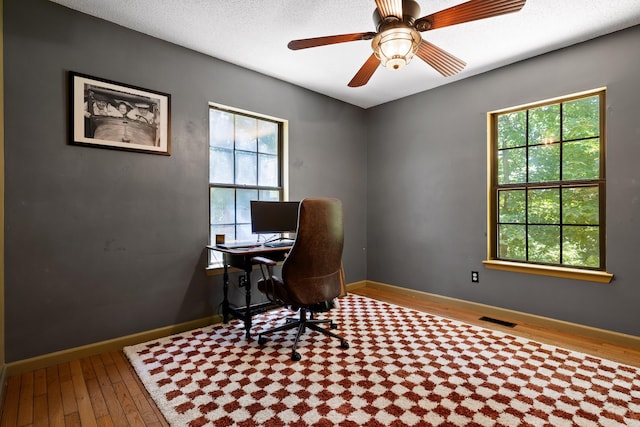 home office with hardwood / wood-style floors, ceiling fan, and a textured ceiling