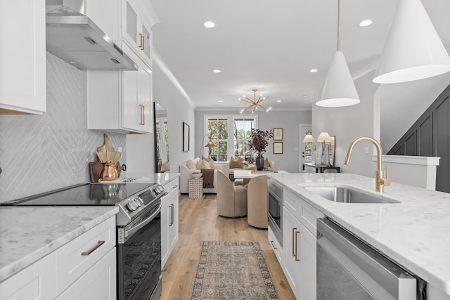 kitchen with pendant lighting, wall chimney range hood, sink, white cabinetry, and stainless steel appliances