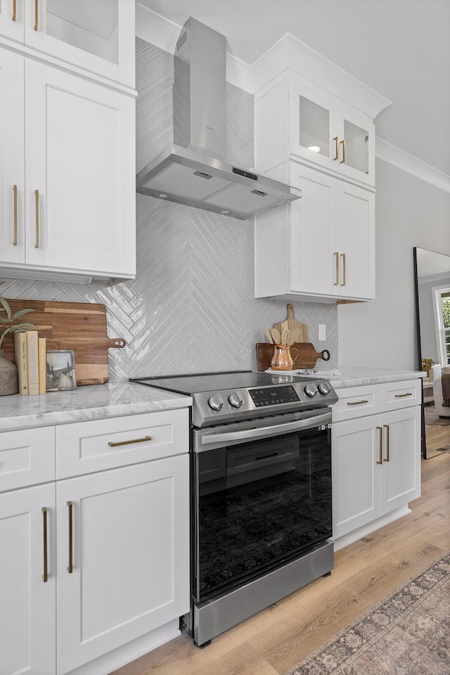 kitchen featuring white cabinets, wall chimney range hood, decorative backsplash, stainless steel electric range oven, and light stone counters