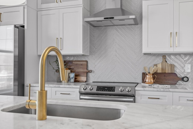 kitchen with light stone counters, white cabinets, wall chimney range hood, and appliances with stainless steel finishes