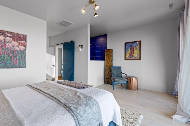 bedroom with light hardwood / wood-style floors, connected bathroom, and a barn door