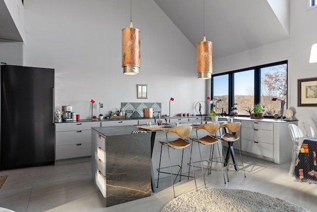 kitchen with high end black fridge, white cabinetry, high vaulted ceiling, and hanging light fixtures