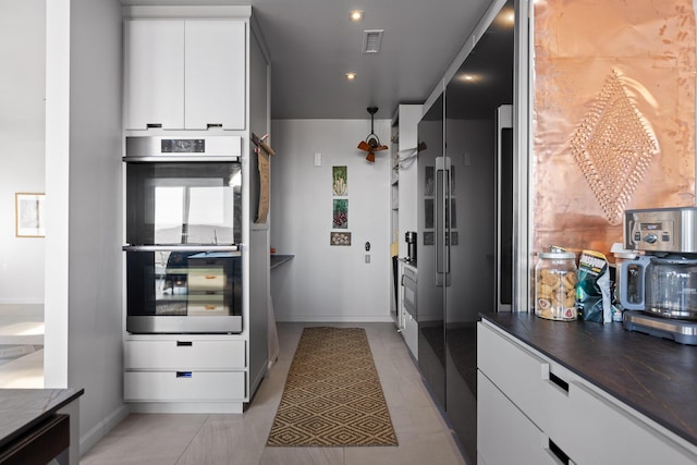 kitchen featuring light tile patterned floors, stainless steel double oven, white cabinets, and high end black refrigerator