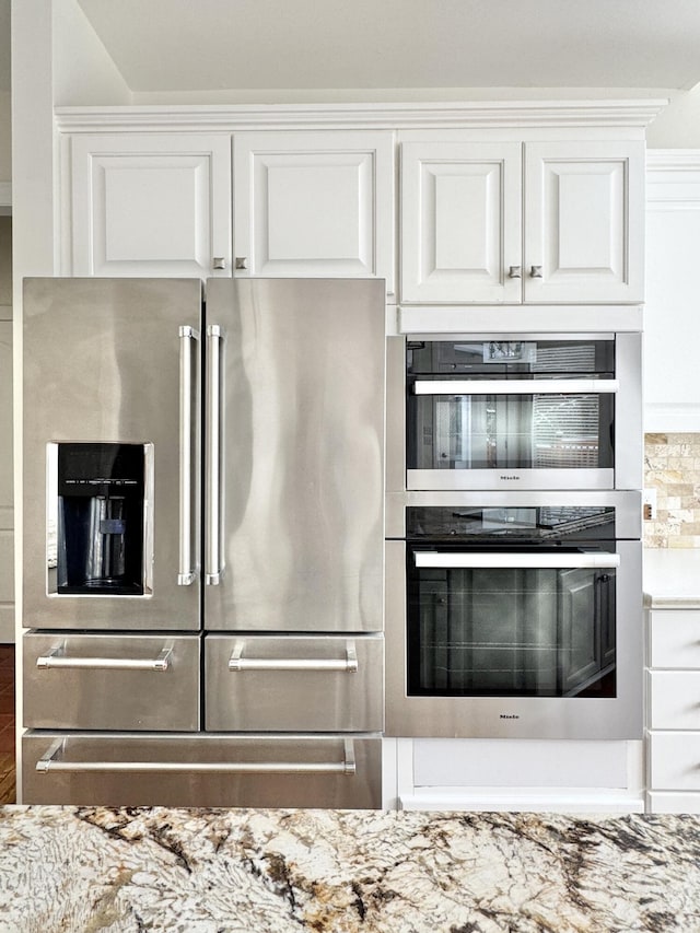 kitchen featuring white cabinets, wood-type flooring, stainless steel appliances, and light stone countertops