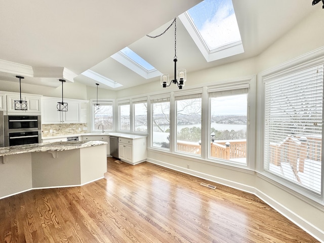 kitchen with light stone countertops, lofted ceiling with skylight, a chandelier, white cabinets, and appliances with stainless steel finishes