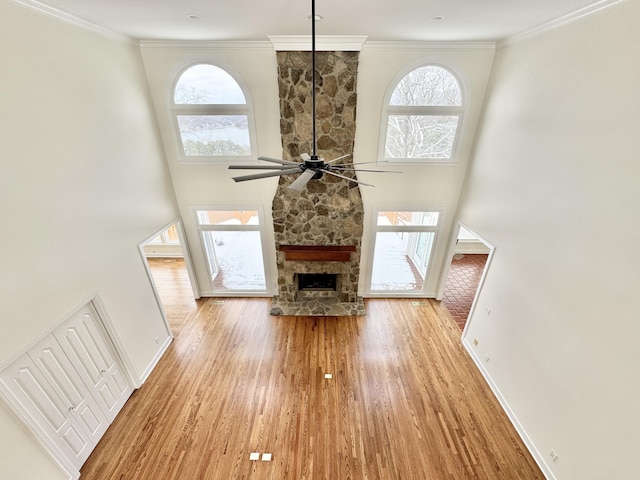 unfurnished living room featuring a high ceiling, crown molding, ceiling fan, a fireplace, and light hardwood / wood-style floors