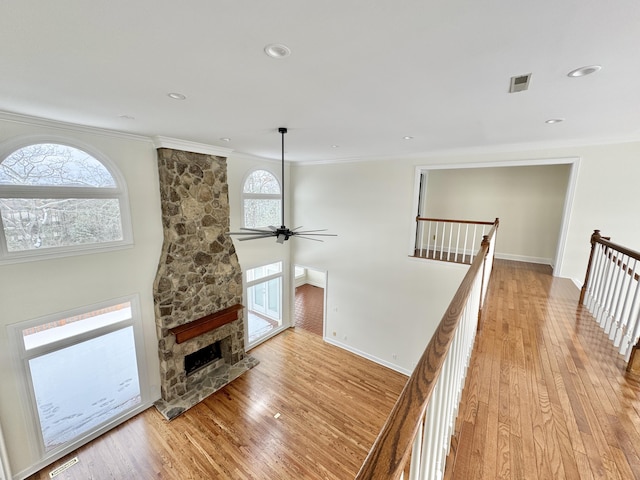 living room featuring light hardwood / wood-style floors, a stone fireplace, ceiling fan, and crown molding