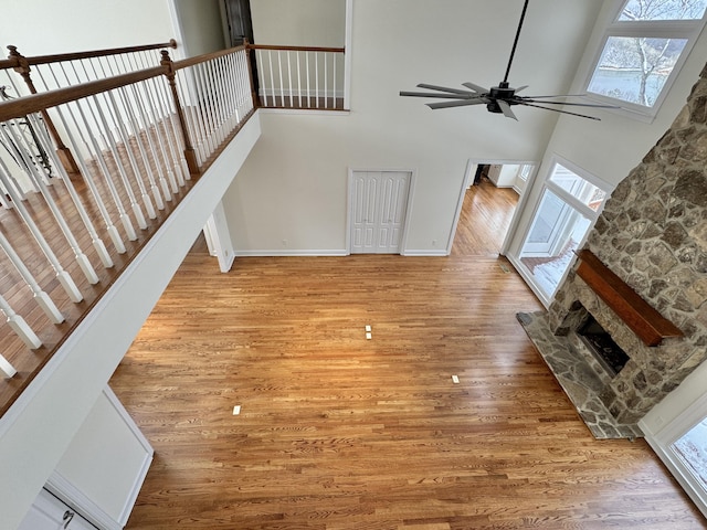 unfurnished living room featuring ceiling fan, light hardwood / wood-style floors, a stone fireplace, and a high ceiling