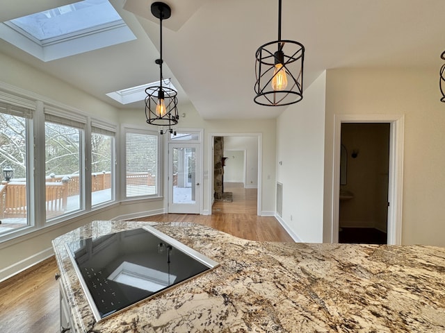 kitchen with pendant lighting, lofted ceiling with skylight, light stone countertops, and light hardwood / wood-style flooring