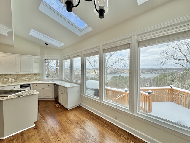 kitchen featuring white cabinetry, stainless steel dishwasher, backsplash, a chandelier, and vaulted ceiling with skylight