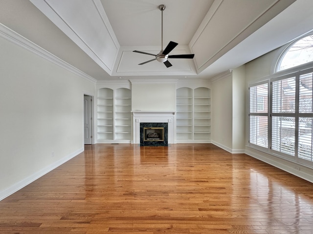 unfurnished living room featuring built in shelves, ceiling fan, a raised ceiling, and ornamental molding