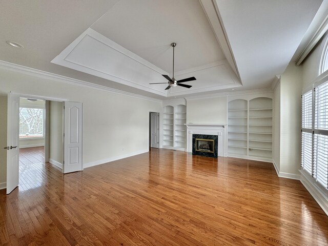 unfurnished living room featuring ornamental molding, ceiling fan, wood-type flooring, built in features, and a premium fireplace