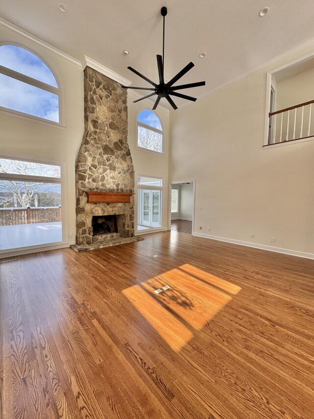 unfurnished living room featuring hardwood / wood-style floors, a healthy amount of sunlight, a stone fireplace, and a towering ceiling