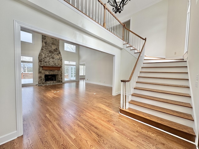 unfurnished living room with a fireplace, a towering ceiling, an inviting chandelier, and hardwood / wood-style flooring