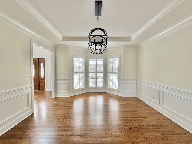 unfurnished dining area featuring a tray ceiling, crown molding, hardwood / wood-style floors, and an inviting chandelier