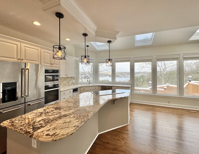 kitchen with appliances with stainless steel finishes, light stone counters, a kitchen island, white cabinetry, and hanging light fixtures