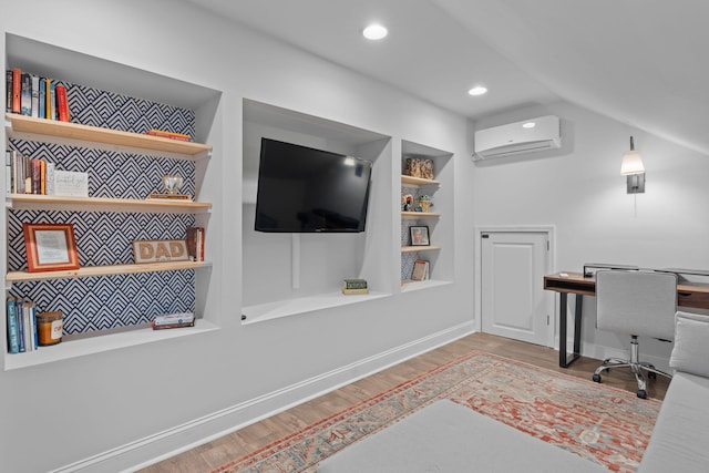 home office with an AC wall unit, built in features, vaulted ceiling, and wood-type flooring